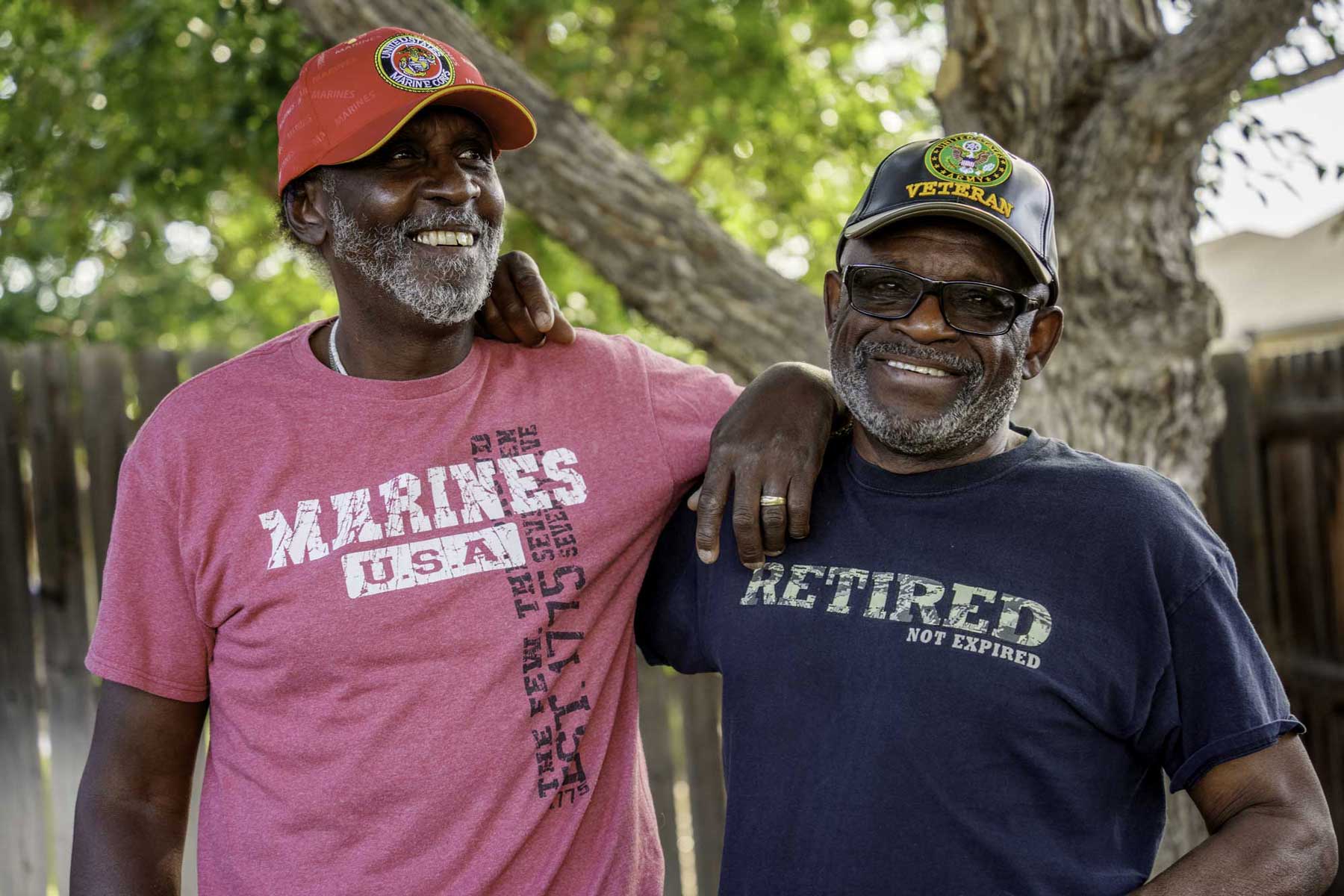 Two older Black veterans smiling outdoors, one wearing a US Marines t-shirt, symbolizing the commitment to civic duty and national service.
